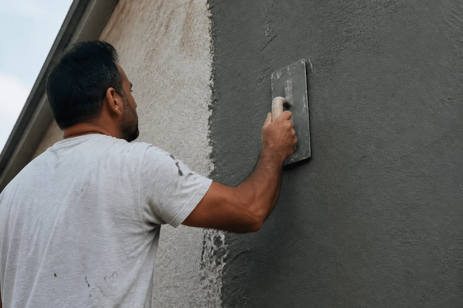 Maçon appliquant revêtement gris sur facade verticale avec truelle