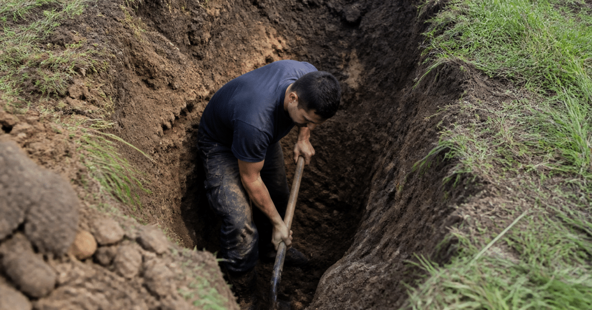 Ouvrier creusant excavation profonde sous terrain herbeux