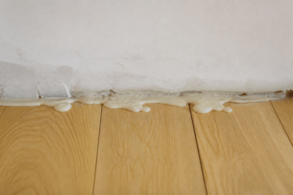 Colle débordant sur parquet clair près mur inégal