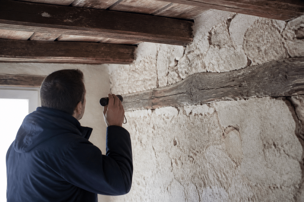 Diagnosticien inspectant murs anciens avec poutres apparentes visibles