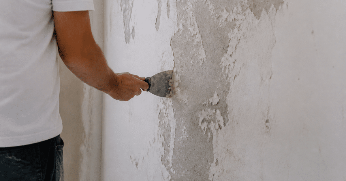 Personne grattant enduit blanc mur intérieur avec outil