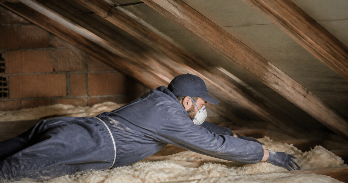 Ouvrier allongé installe isolant fibreux entre solives bois combles