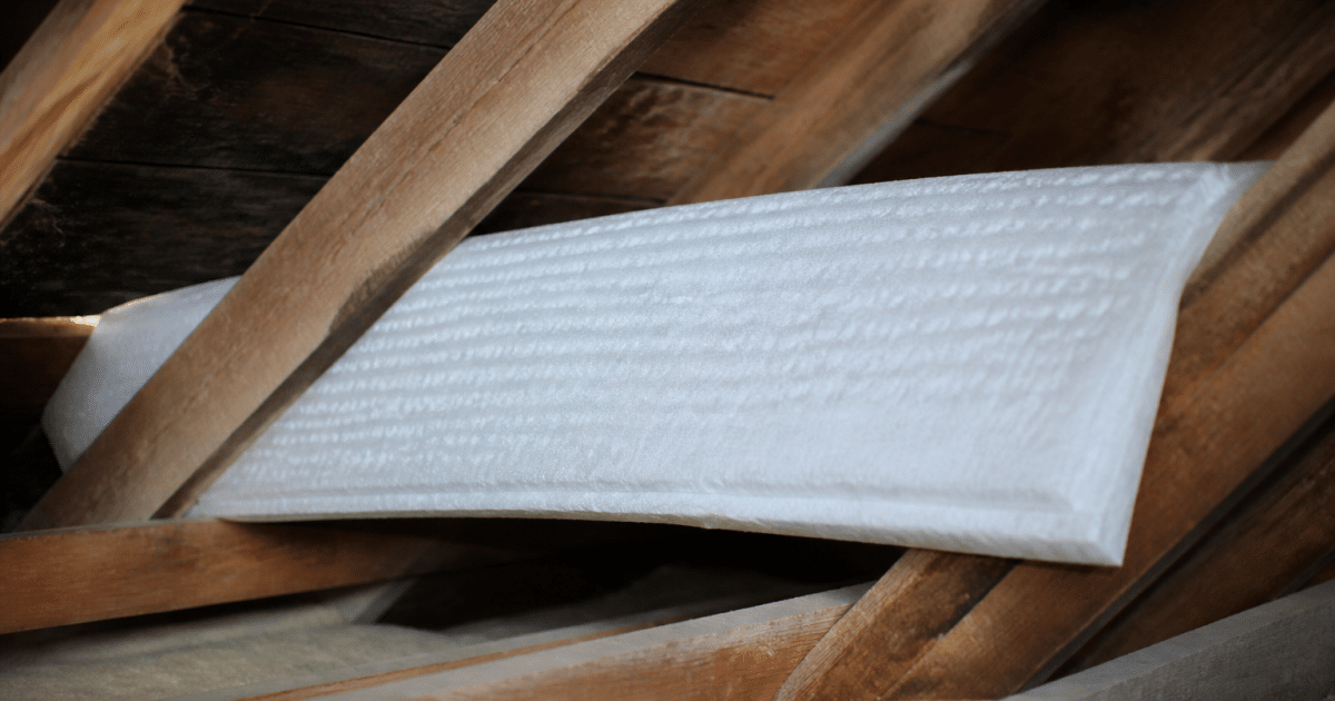 Matelas isolant blanc positionne horizontalement entre poutres de bois inclinées