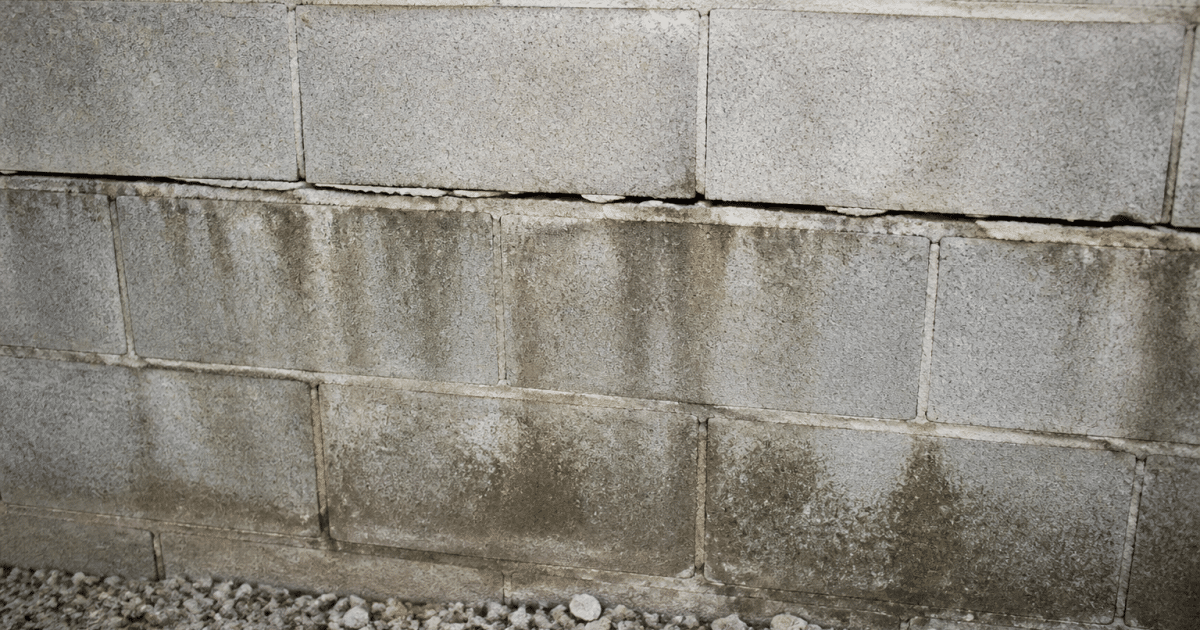 Mur de parpaings gris avec fissure horizontale et infiltration d'eau
