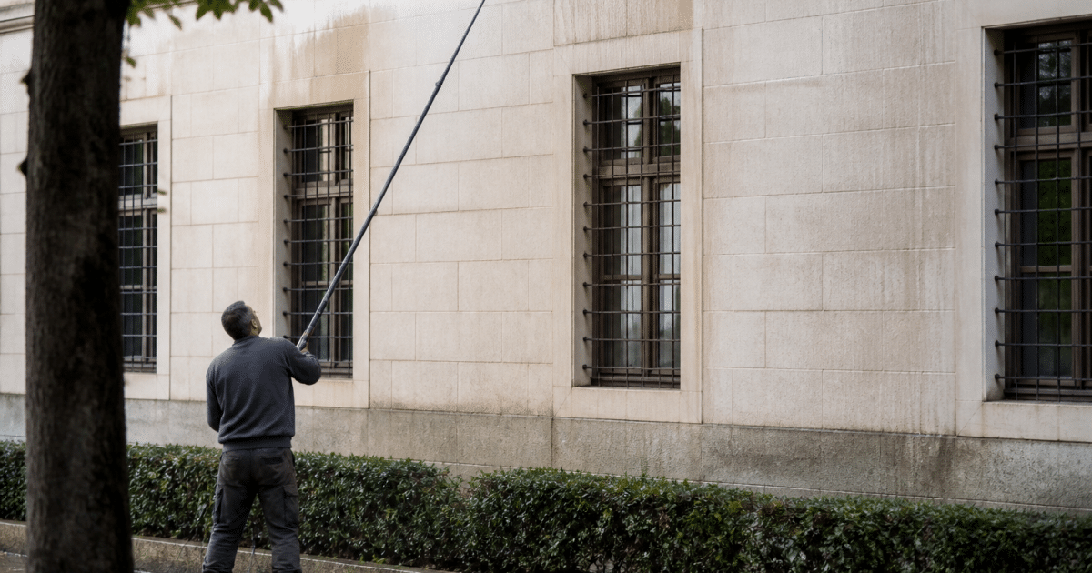 Personne utilisant tuyau long depuis sol pour nettoyer facade