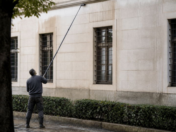 Personne utilisant tuyau long depuis sol pour nettoyer facade