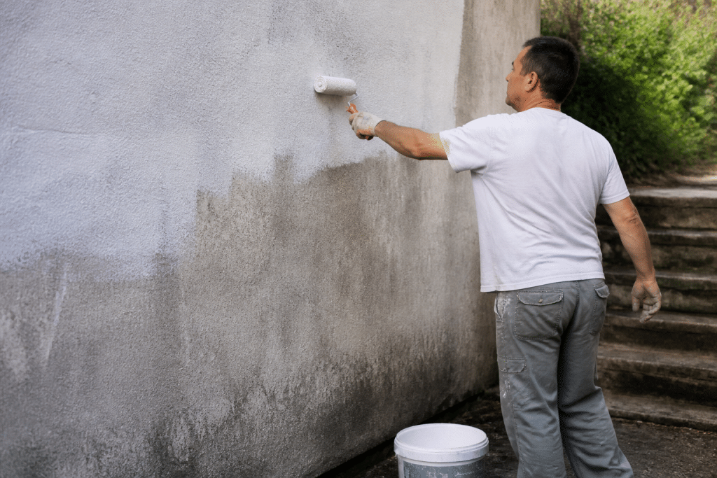 Peintre appliquant peinture hydrofuge blanche sur murs humides