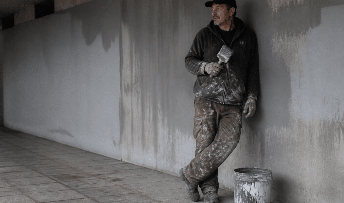 Personne appuyee contre mur souterrain avec pinceau et seau de peinture