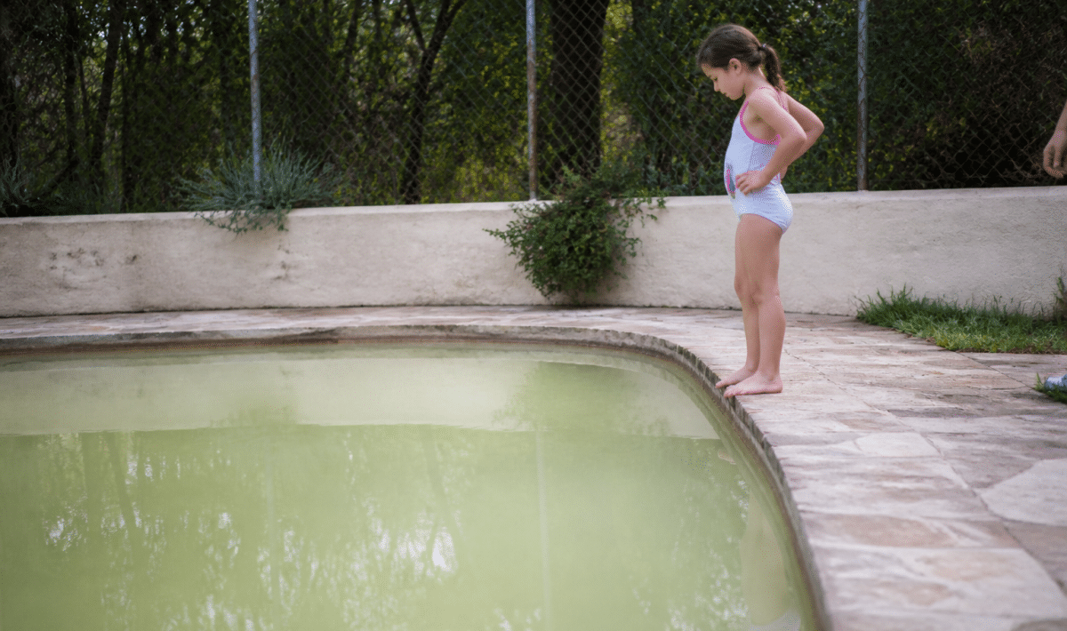 Piscine avec eau trouble et blanchâtre, personne hésitante au bord