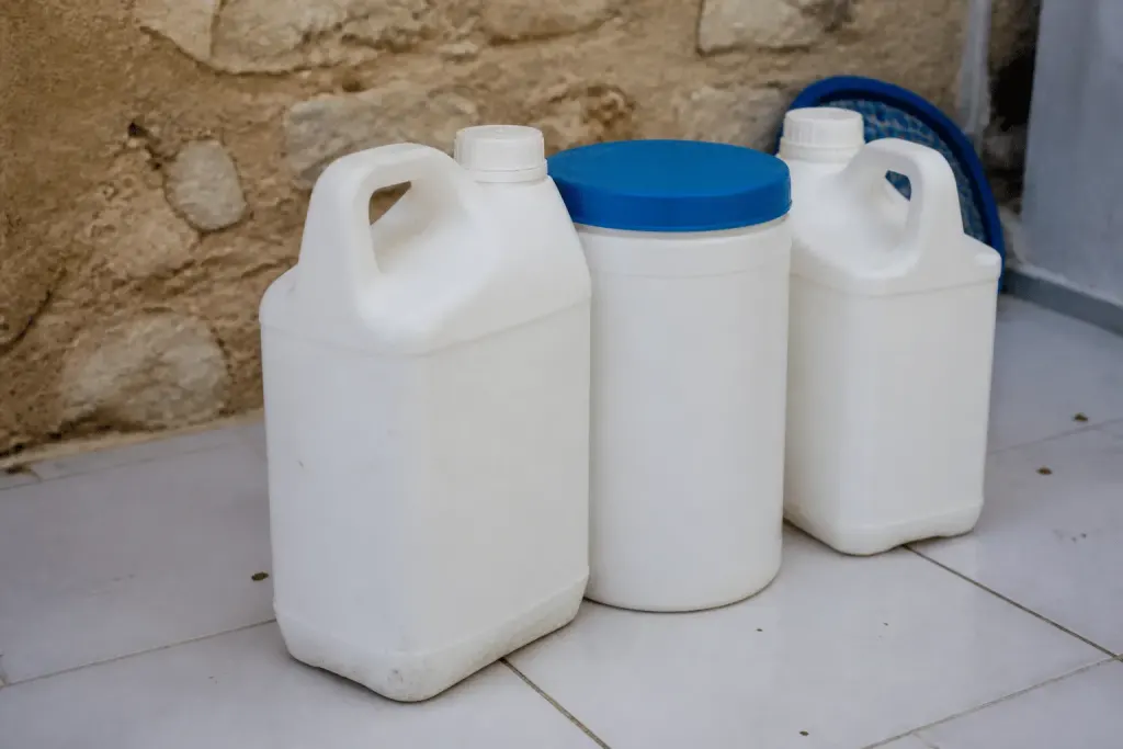 Bouteilles de produits chimiques piscine posées sur carrelage blanc