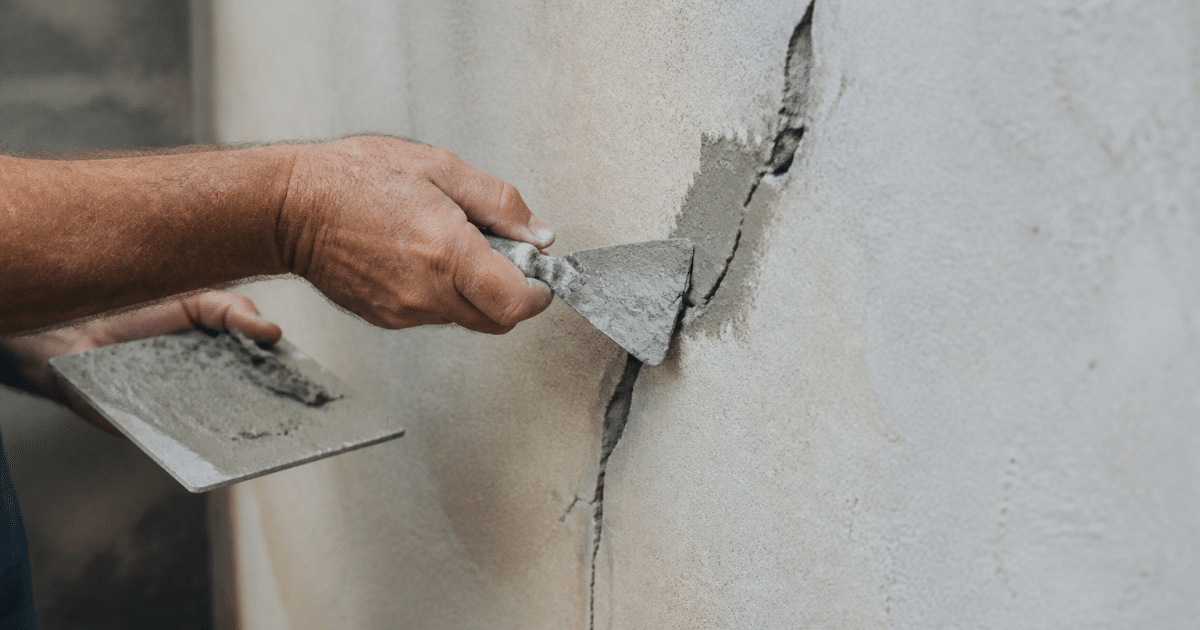 Mains appliquant du mortier sur fissure murale avec spatule