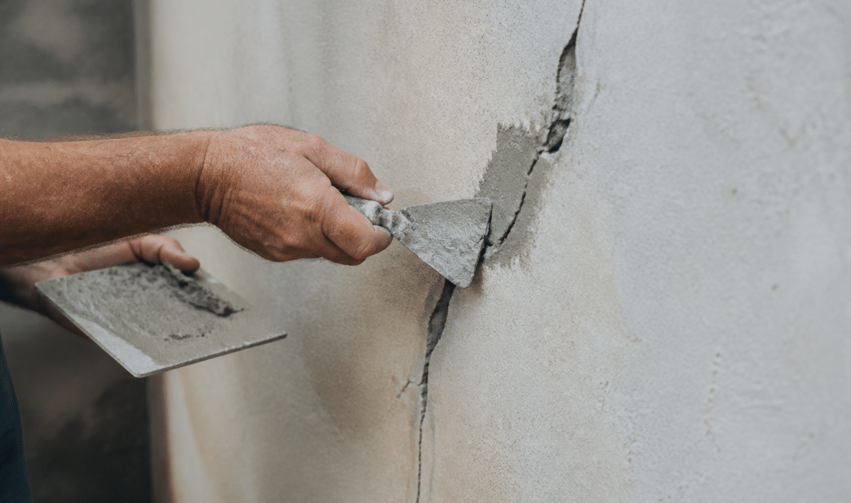 Mains appliquant du mortier sur fissure murale avec spatule