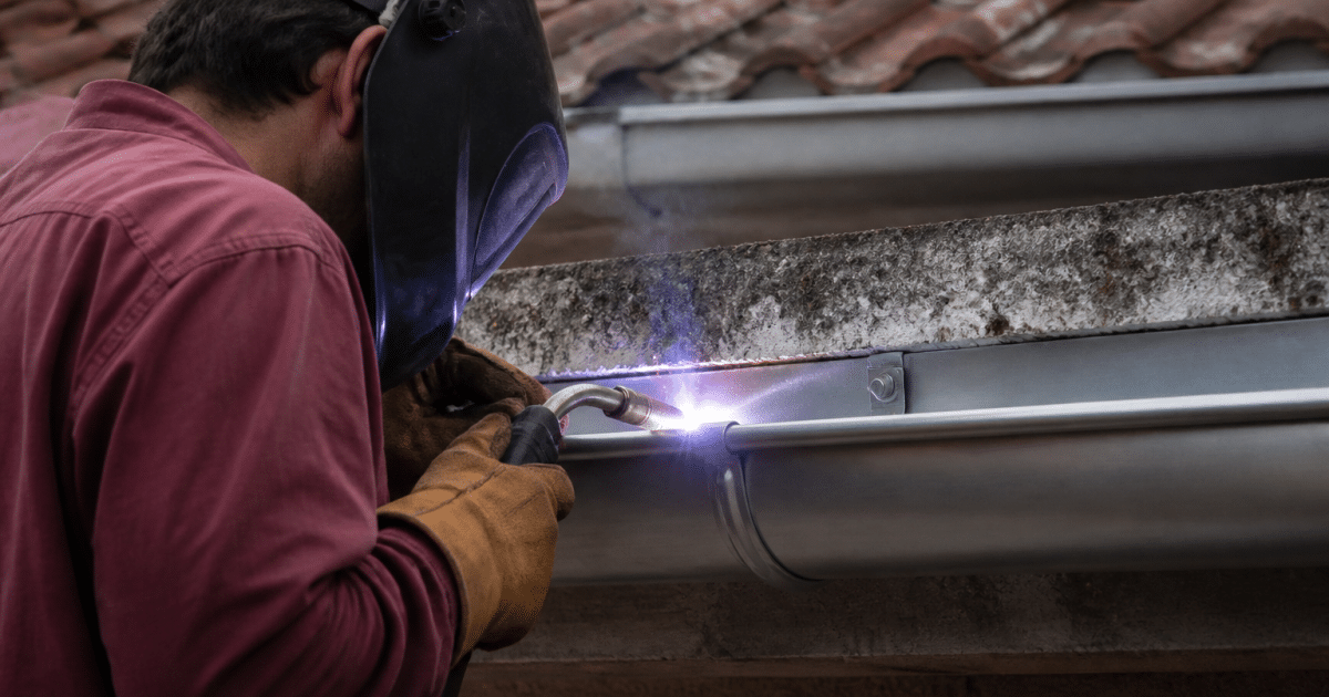 Artisan soudant gouttiere metallique grise horizontalement installee