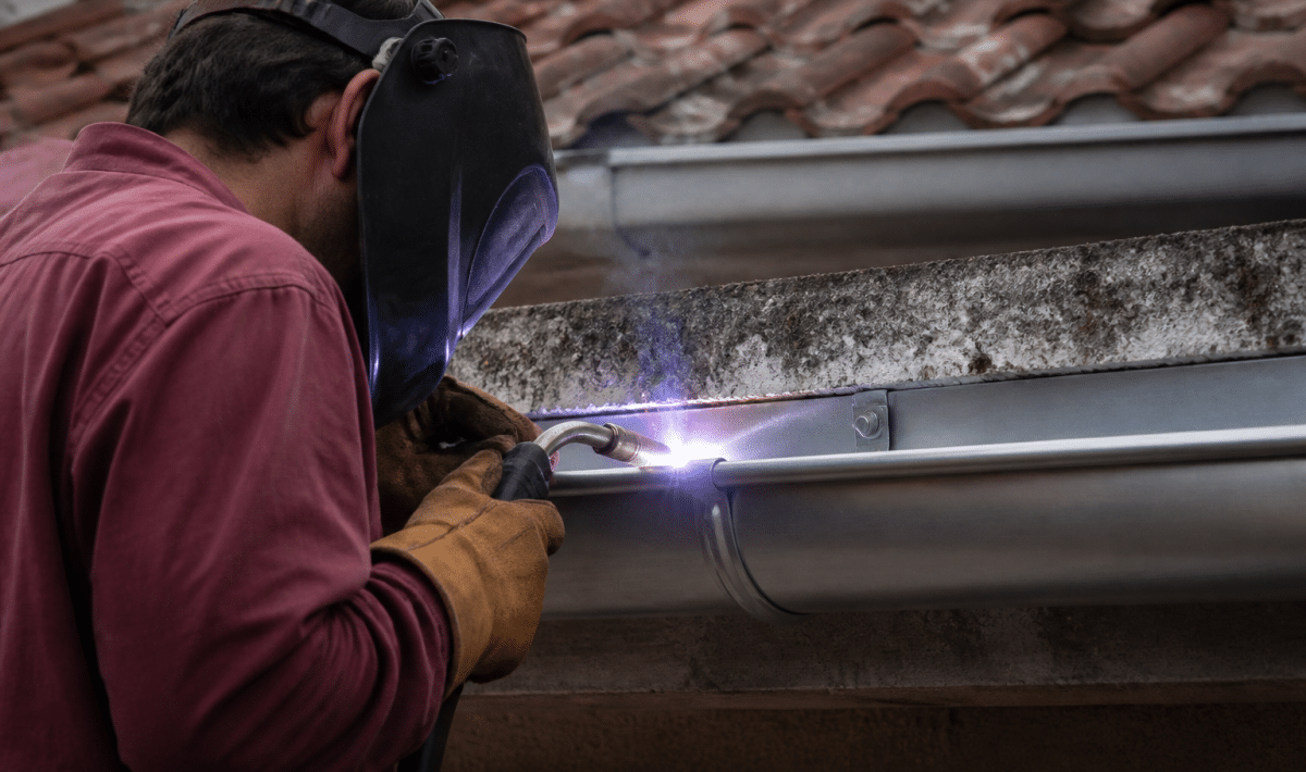 Artisan soudant gouttiere metallique grise horizontalement installee