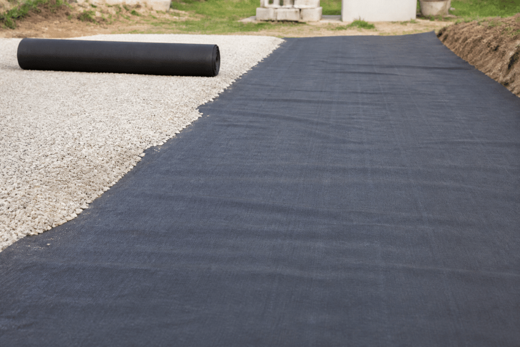Tissu geotextile noir deroulé sur sol nivelé avec gravier
